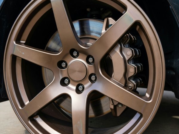 Close natural-light view of an anodized bronze forged 6-spoke wheel clearing a six-piston brake caliper