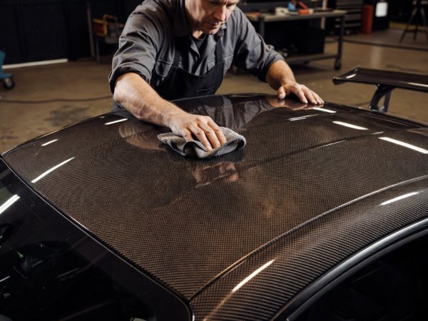 Close view of a custom builder wiping down a bronze-tinted exposed carbon fiber roof panel